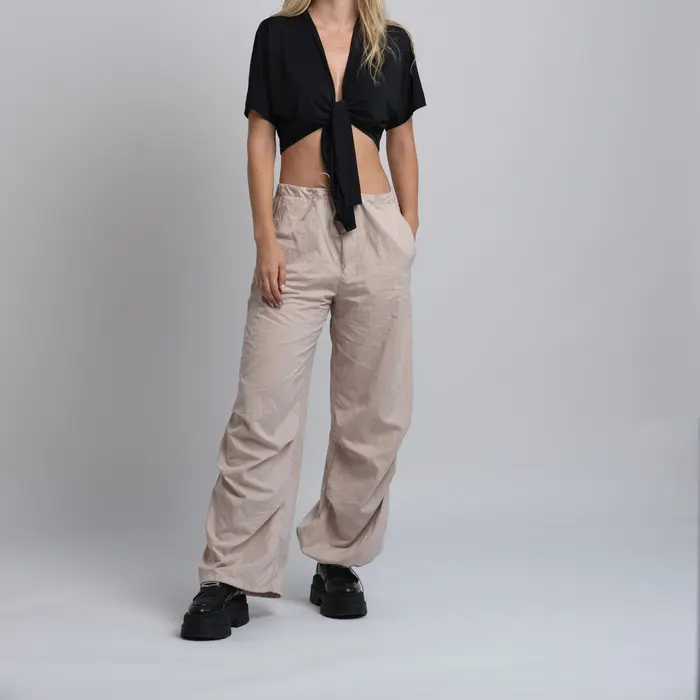 Stone-colored relaxed trousers with black boots on a grey backdrop