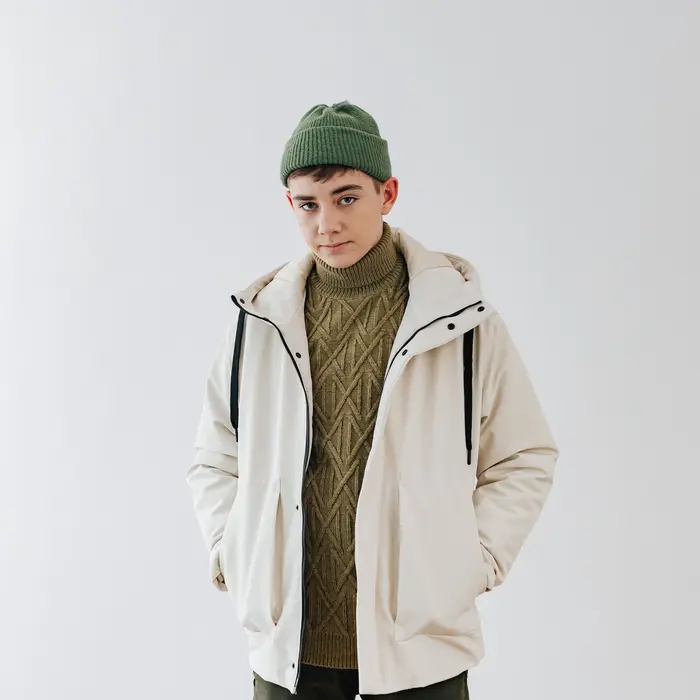 Person in a cream hooded shell jacket and green beanie on a light grey backdrop